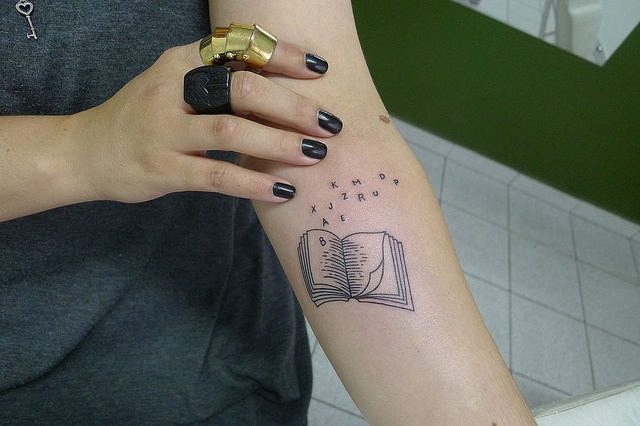 Black letters and book tattoo on arm