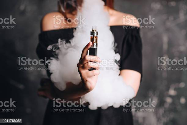 Close-up photo of female holding e-cigarette with smoke. Indoors